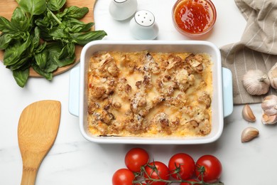 Tasty baked cauliflower, sauce, spices and products on white marble table, flat lay