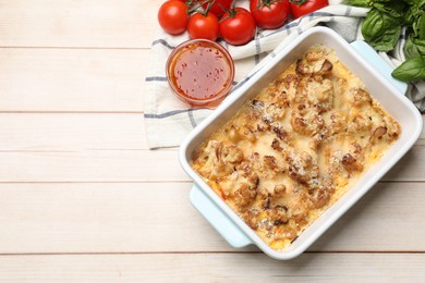 Photo of Tasty baked cauliflower in baking dish, tomatoes, basil and sauce on light wooden table, flat lay. Space for text