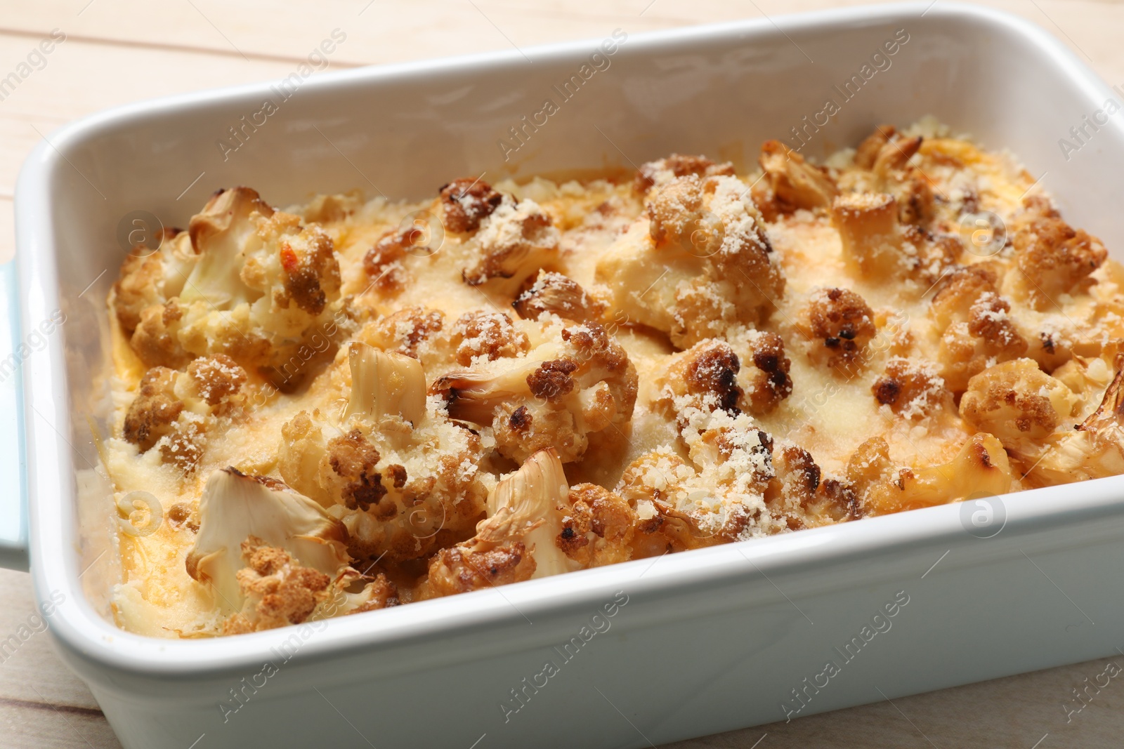 Photo of Tasty baked cauliflower in baking dish on light wooden table, closeup