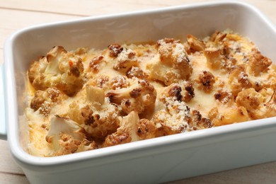 Tasty baked cauliflower in baking dish on light wooden table, closeup