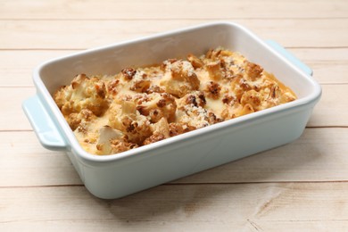 Tasty baked cauliflower in baking dish on light wooden table, closeup