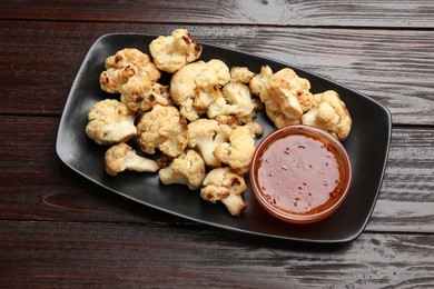 Tasty baked cauliflower with sauce on wooden table, top view