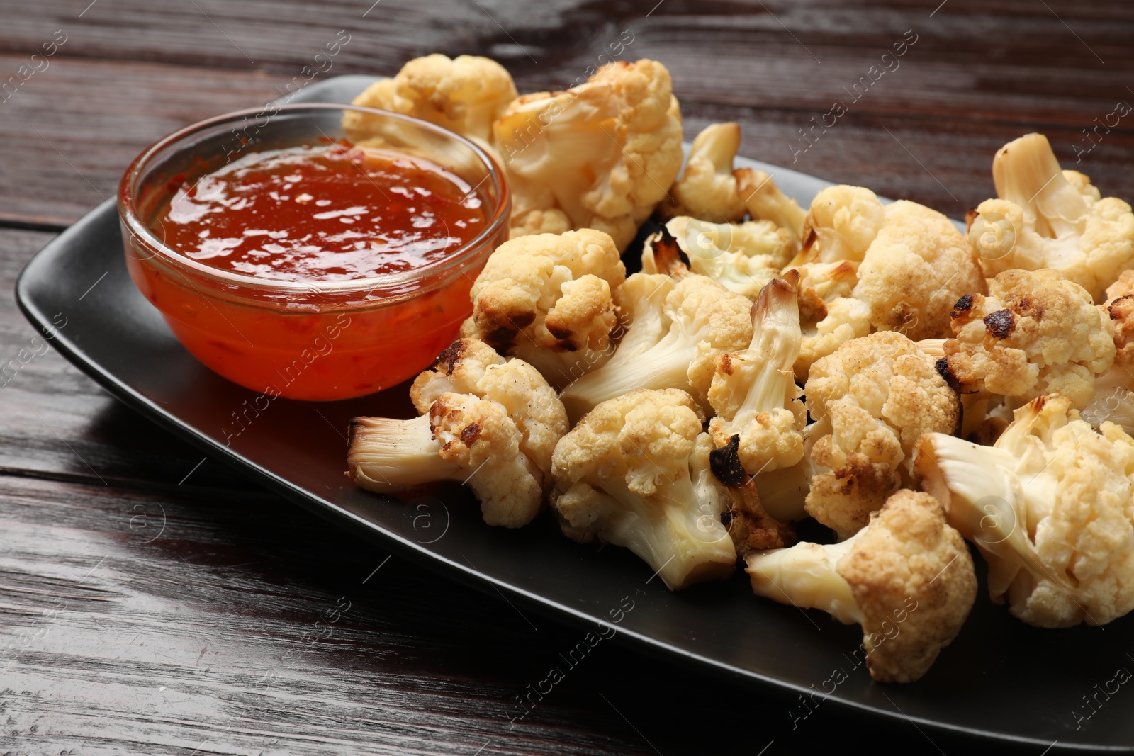 Photo of Tasty baked cauliflower with sauce on wooden table, closeup