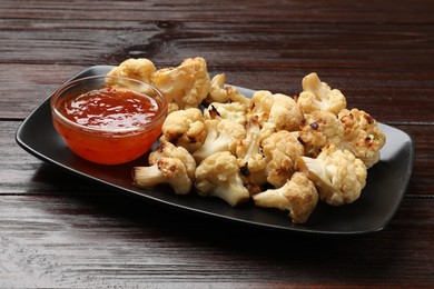 Photo of Tasty baked cauliflower with sauce on wooden table, closeup