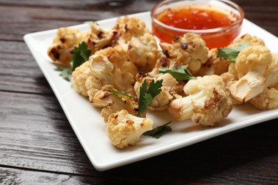 Photo of Tasty baked cauliflower with parsley and sauce on wooden table, closeup