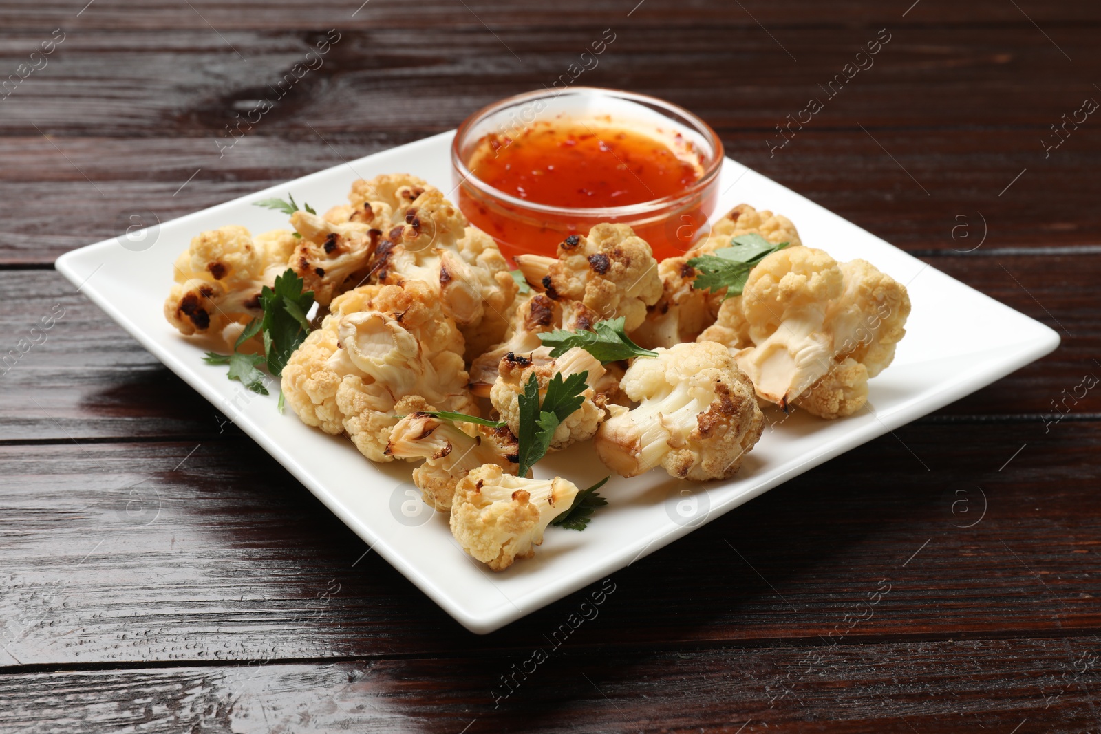 Photo of Tasty baked cauliflower with parsley and sauce on wooden table, closeup