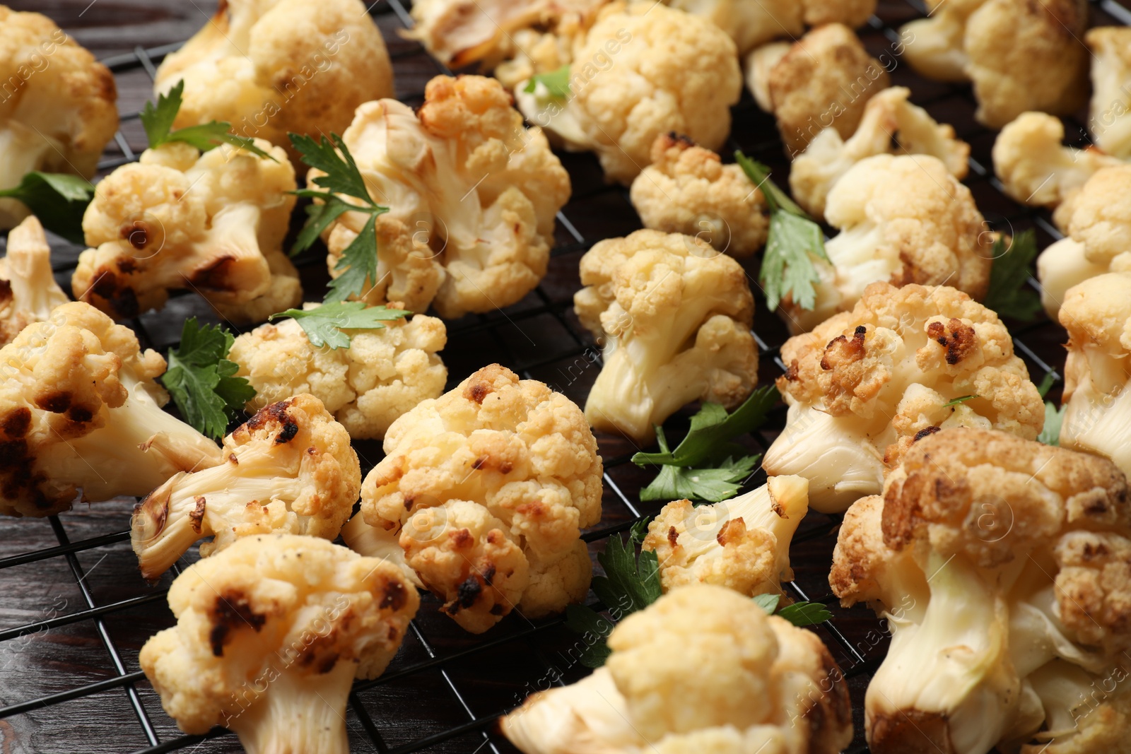 Photo of Cooling rack with tasty baked cauliflower and parsley on wooden table, closeup