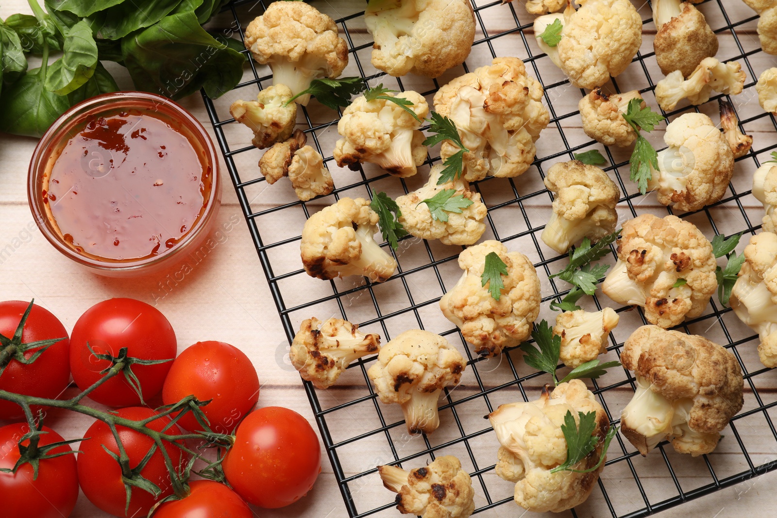 Photo of Cooling rack with tasty baked cauliflower, sauce and products on light wooden table, flat lay