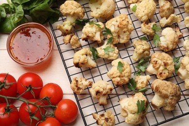 Photo of Cooling rack with tasty baked cauliflower, sauce and products on light wooden table, flat lay