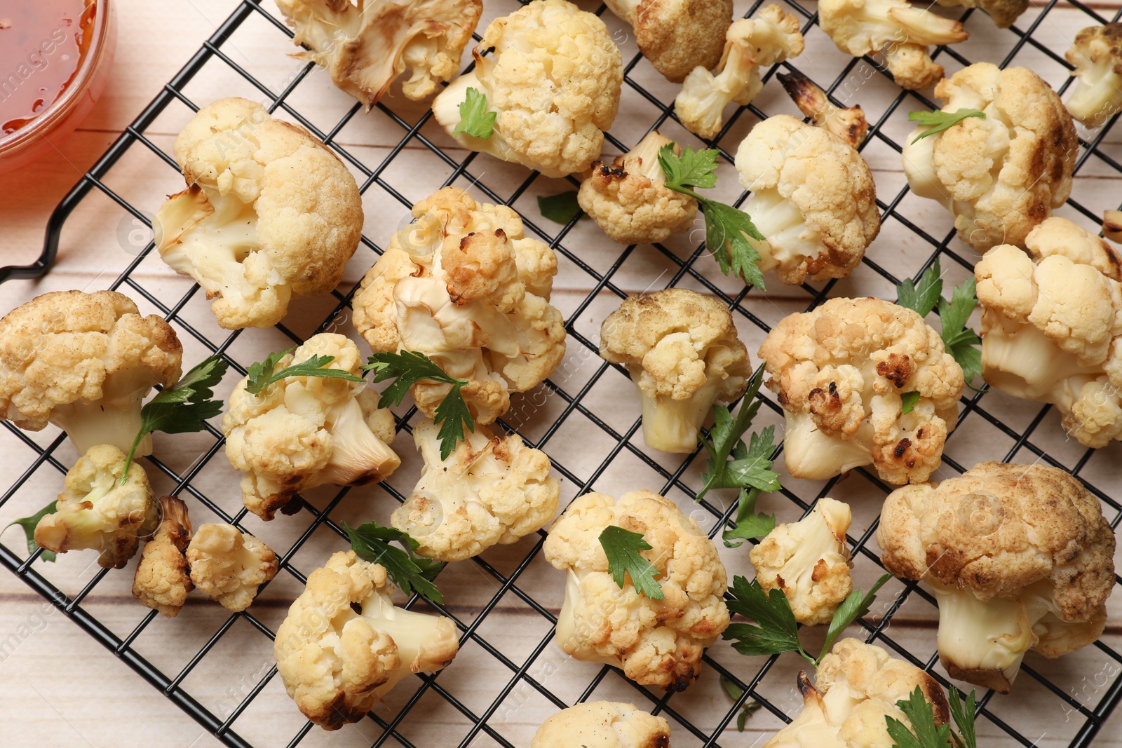 Photo of Cooling rack with tasty baked cauliflower and parsley on light wooden table, top view