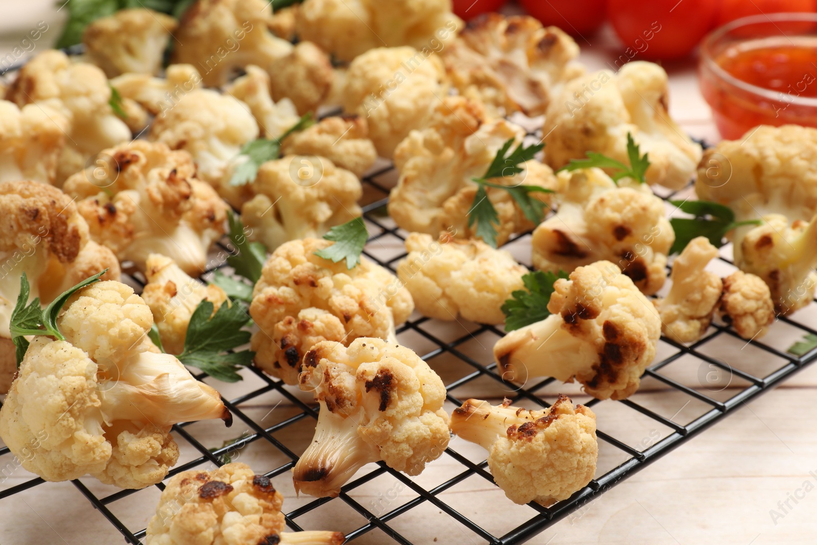 Photo of Cooling rack with tasty baked cauliflower and parsley on light wooden table, closeup