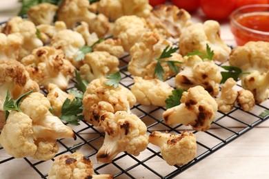 Cooling rack with tasty baked cauliflower and parsley on light wooden table, closeup