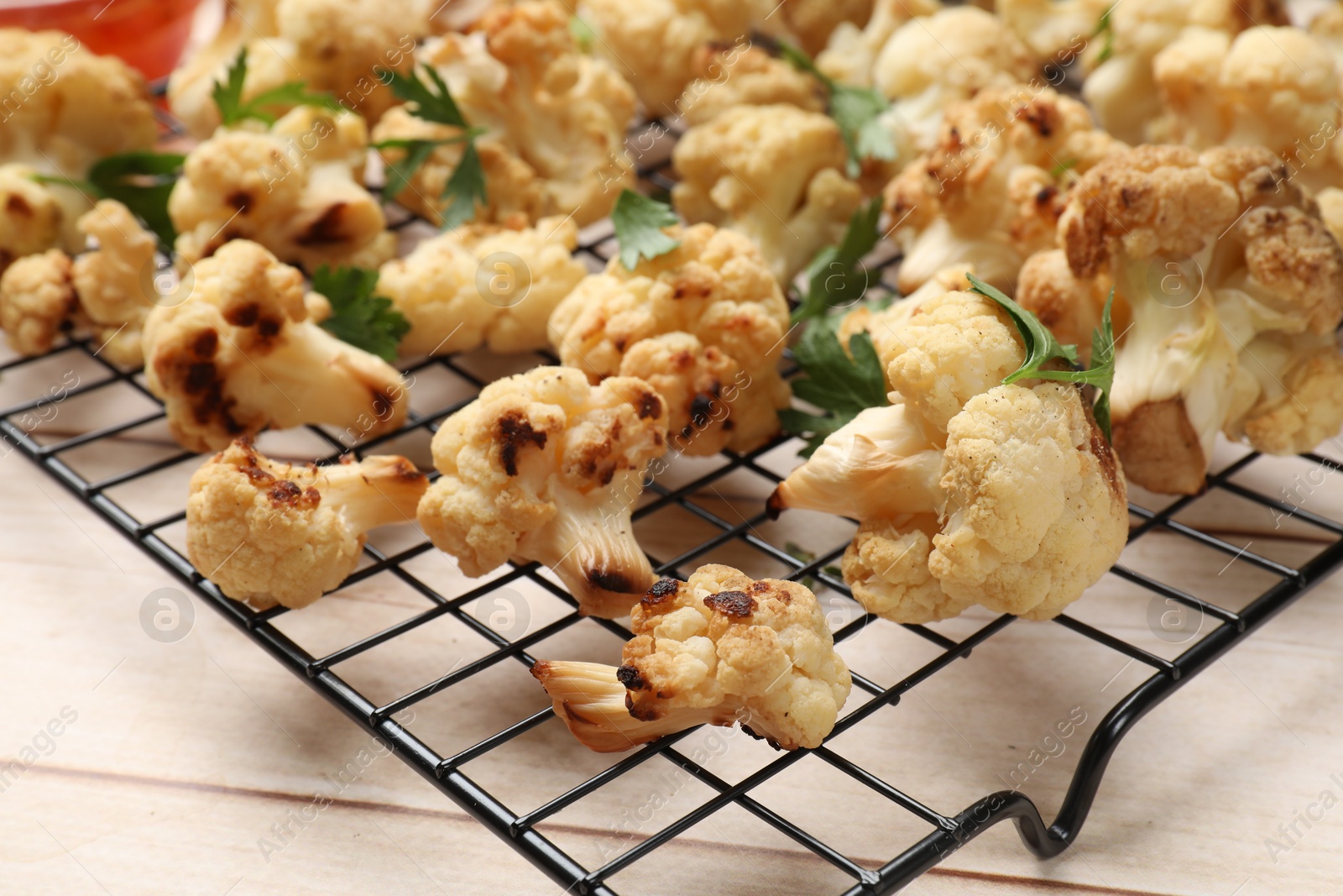 Photo of Cooling rack with tasty baked cauliflower and parsley on light wooden table, closeup