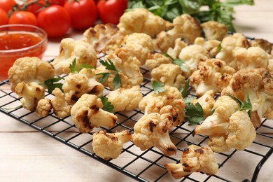 Photo of Cooling rack with tasty baked cauliflower and parsley on light wooden table, closeup