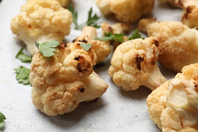 Photo of Tasty baked cauliflower and parsley on parchment, closeup