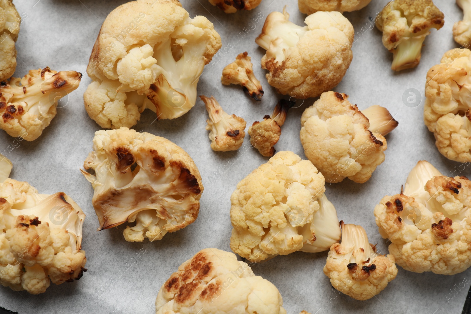 Photo of Tasty baked cauliflower on parchment, flat lay