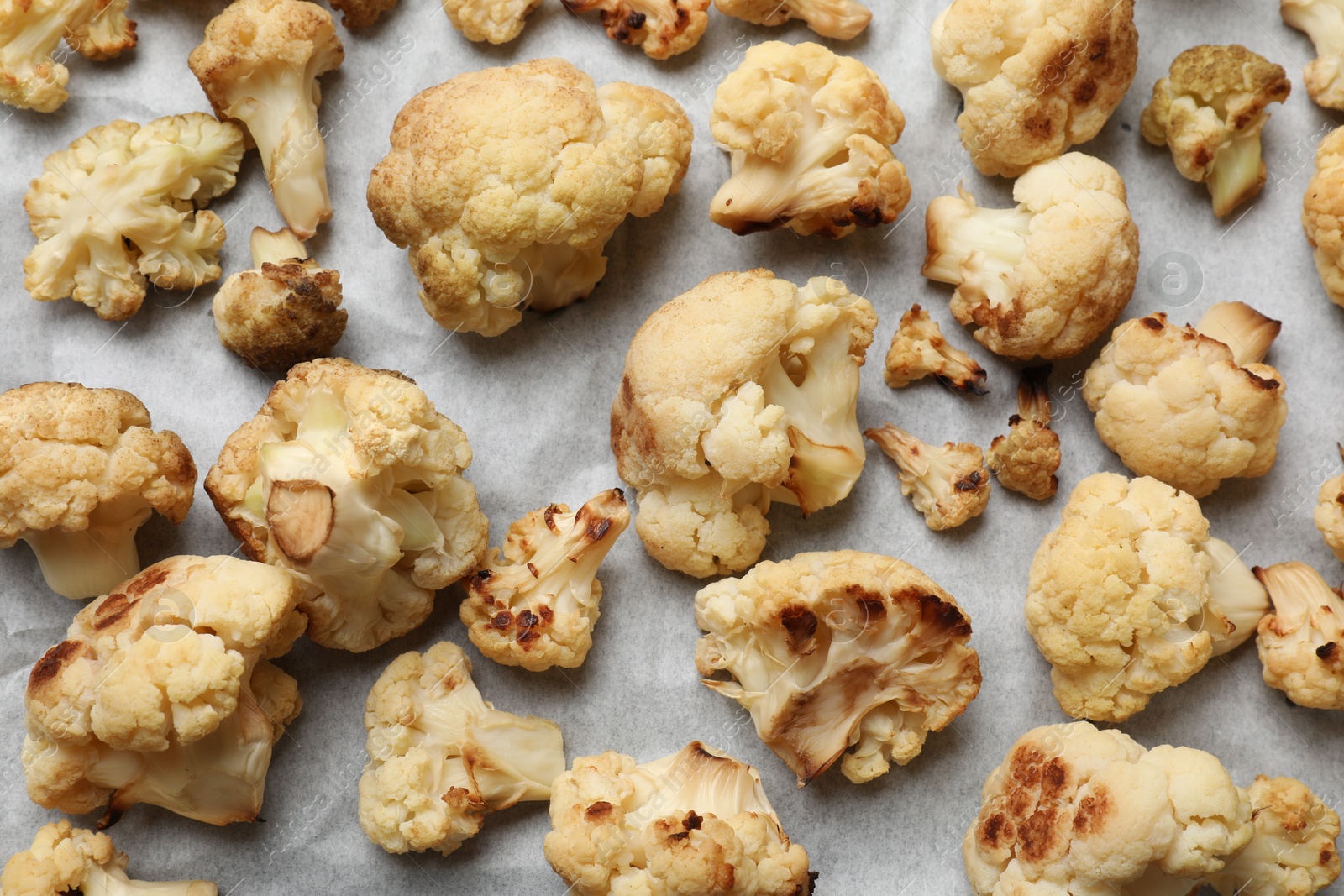 Photo of Tasty baked cauliflower on parchment, flat lay