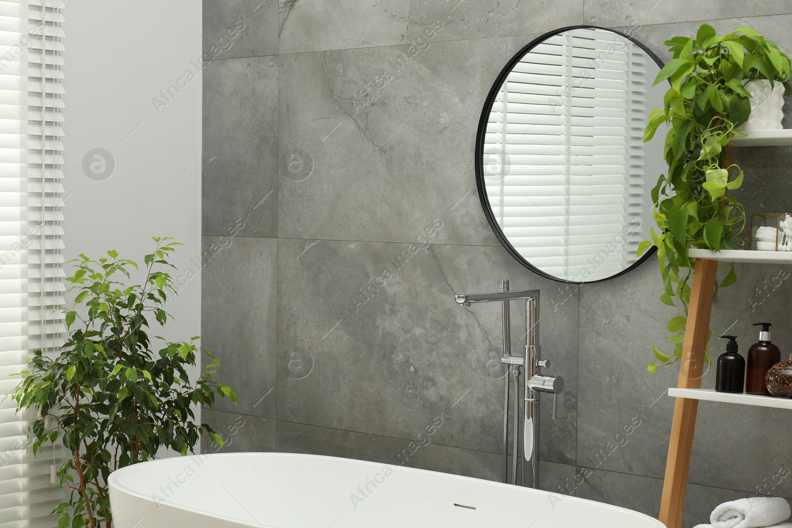 Photo of Round mirror on grey tiled wall over tub in bathroom