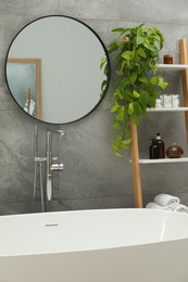 Photo of Round mirror on grey tiled wall over tub in bathroom