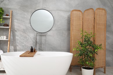 Photo of Wooden folding screen, bathtub, houseplants and mirror in bathroom. Interior design