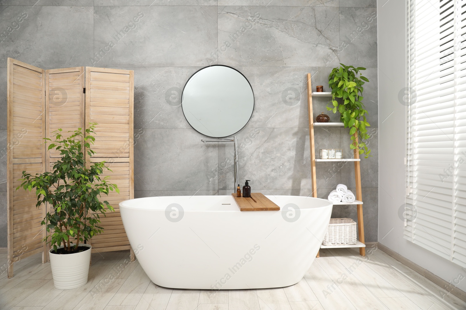 Photo of Wooden folding screen, bathtub, houseplants and mirror in bathroom. Interior design