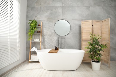 Photo of Wooden folding screen, bathtub, houseplants and mirror in bathroom. Interior design