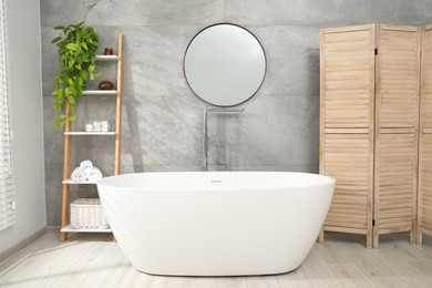 Photo of Wooden folding screen, bathtub, houseplant and mirror in bathroom. Interior design