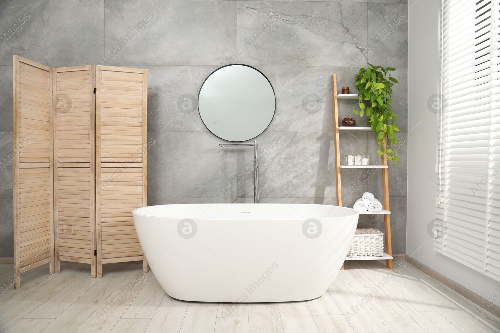 Photo of Wooden folding screen, bathtub, houseplant and mirror in bathroom. Interior design