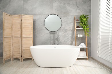 Photo of Wooden folding screen, bathtub, houseplant and mirror in bathroom. Interior design