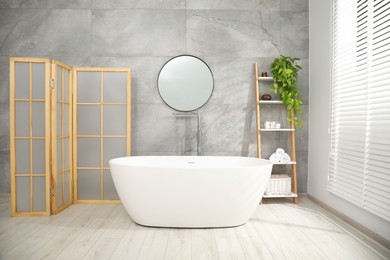 Photo of Folding screen, bathtub, houseplant and mirror in bathroom. Interior design