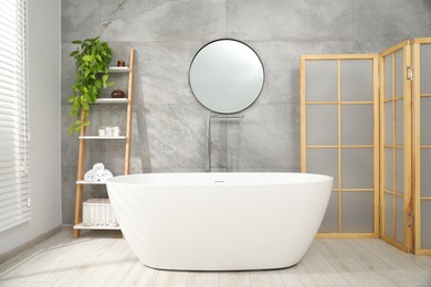 Photo of Folding screen, bathtub, houseplant and mirror in bathroom. Interior design