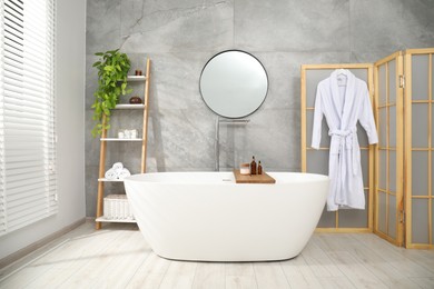 Photo of Folding screen, bathtub, houseplant and mirror in bathroom. Interior design