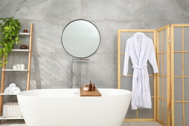 Photo of Folding screen, bathtub, houseplant and mirror in bathroom. Interior design