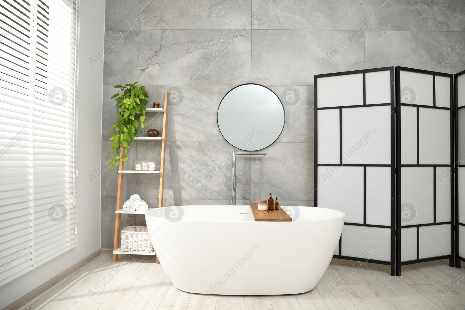 Photo of Folding screen, bathtub, houseplant and mirror in bathroom. Interior design