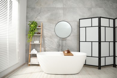 Photo of Folding screen, bathtub, houseplant and mirror in bathroom. Interior design