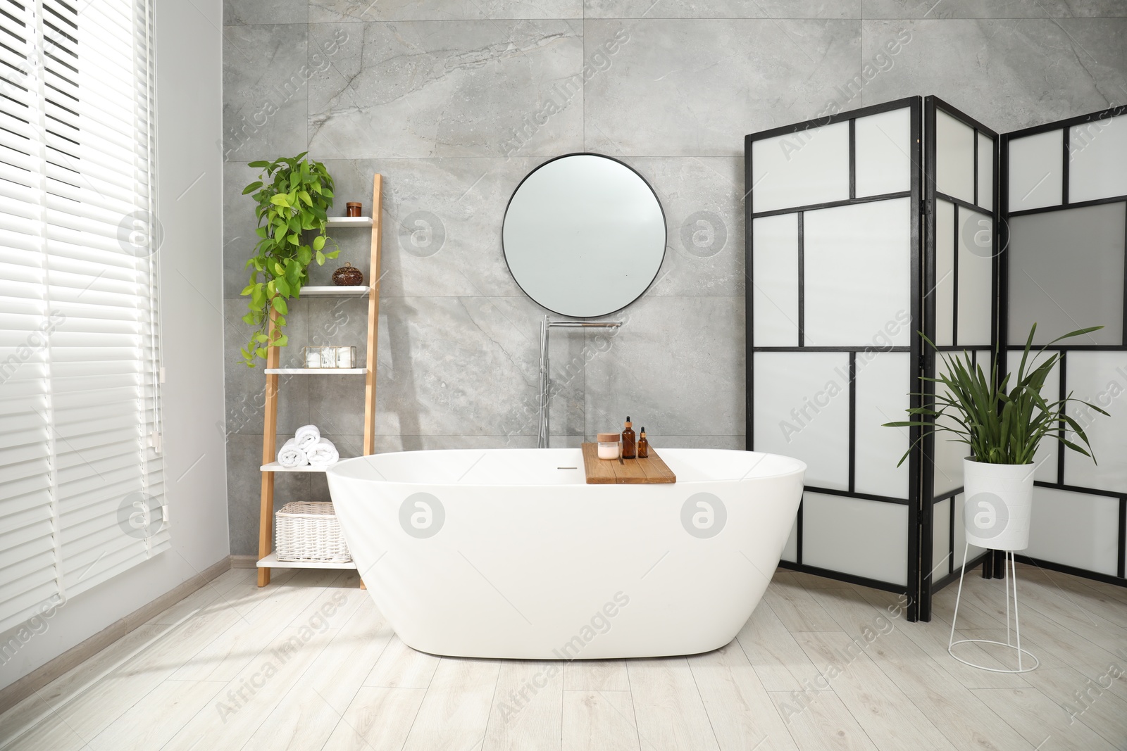 Photo of Folding screen, bathtub, houseplants and mirror in bathroom. Interior design