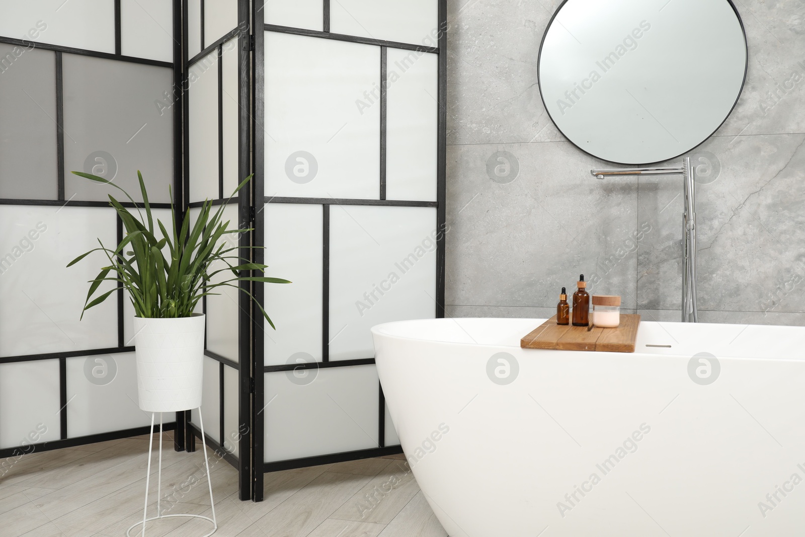 Photo of Folding screen, bathtub, houseplant and mirror in bathroom. Interior design