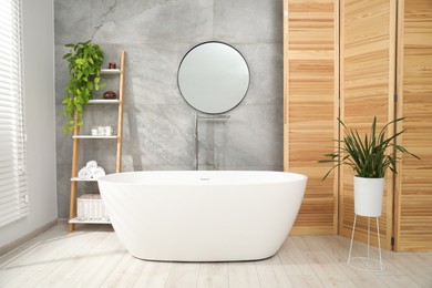 Photo of Wooden folding screen, bathtub, houseplants and mirror in bathroom. Interior design