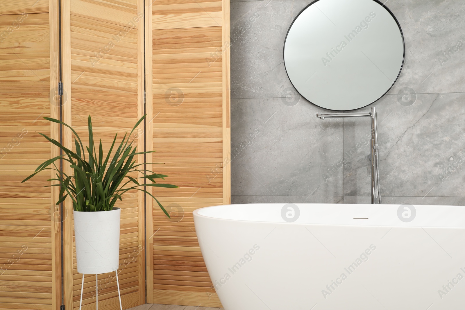 Photo of Wooden folding screen, bathtub, houseplant and mirror in bathroom. Interior design