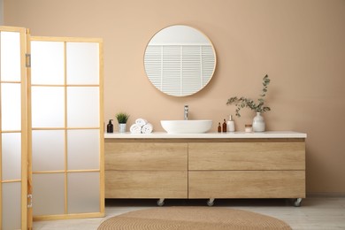 Photo of Folding screen, vanity, sink, mirror and floral decor in bathroom. Interior design