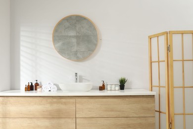 Photo of Folding screen and round mirror over sink in bathroom. Interior design