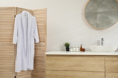 Photo of Stylish bathroom with folding screen and round mirror over sink. Interior design