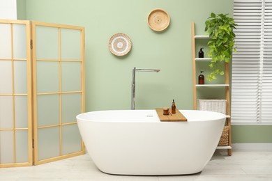 Photo of Stylish bathroom interior with folding screen and tub