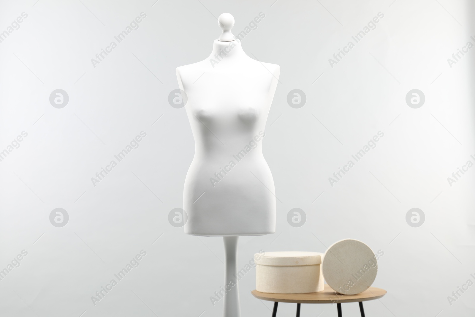 Photo of Mannequin and boxes on side table against light grey background. Fashion designer`s equipment