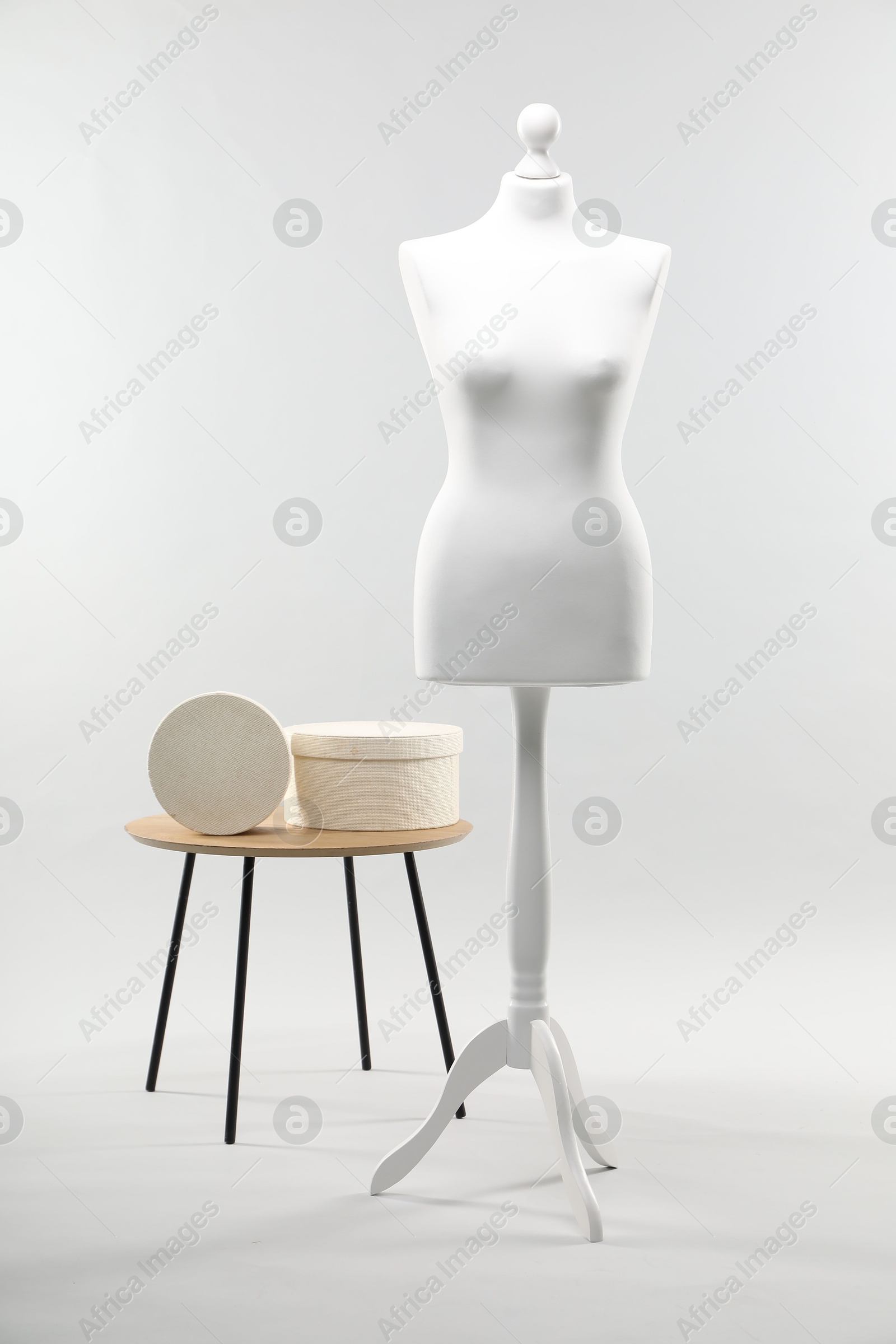 Photo of Mannequin and boxes on side table against light grey background. Fashion designer`s equipment