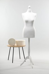 Photo of Mannequin and boxes on side table against light grey background. Fashion designer`s equipment