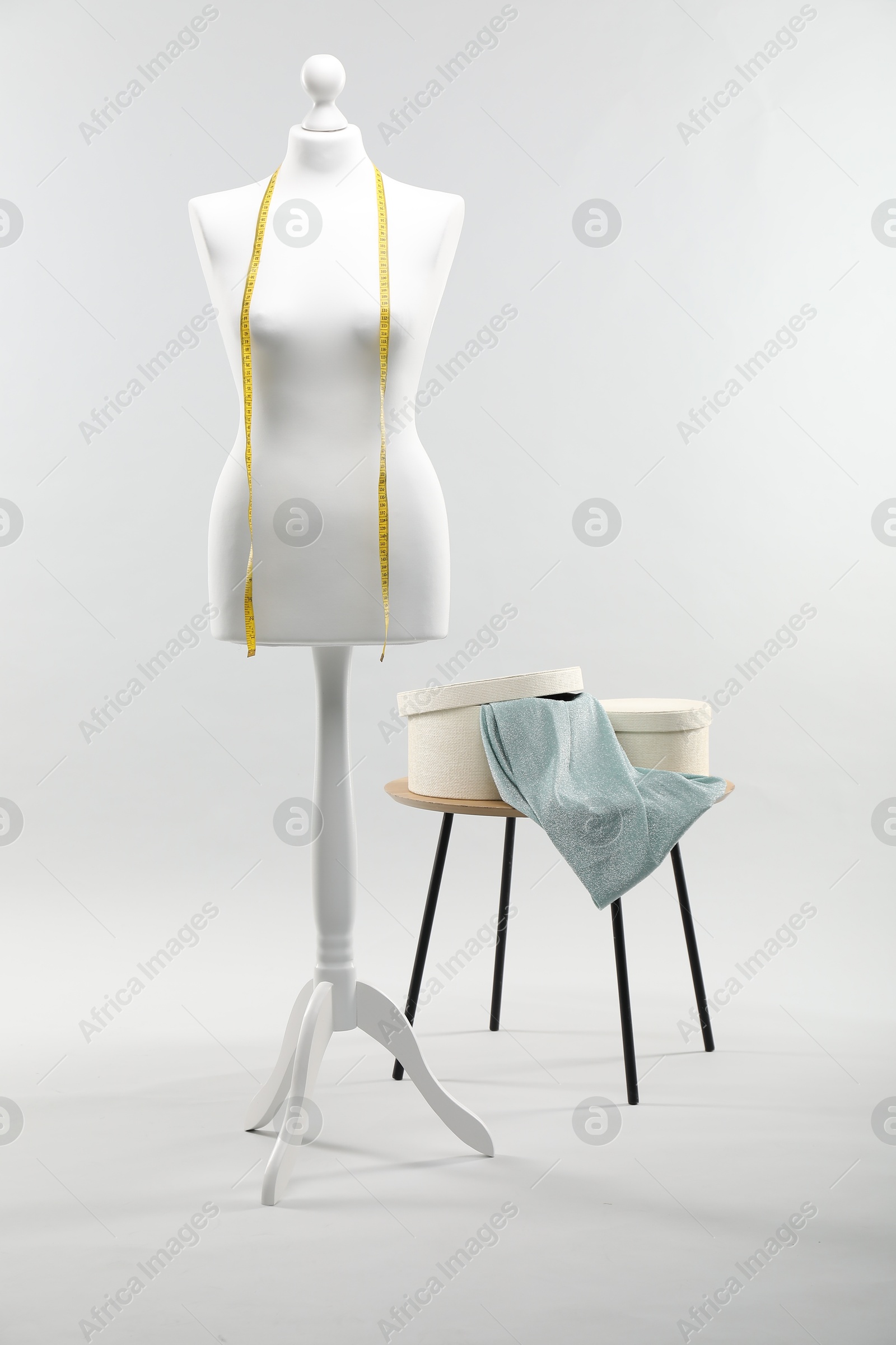 Photo of Mannequin with measuring tape and fabric in boxes on side table against light grey background