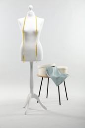 Photo of Mannequin with measuring tape and fabric in boxes on side table against light grey background