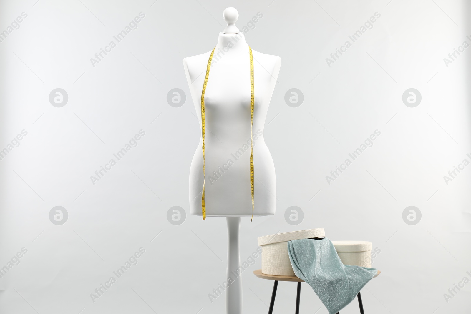 Photo of Mannequin with measuring tape and fabric in boxes on side table against light grey background