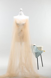 Photo of Mannequin with fabric and boxes on side table against light grey background. Creating new outfit